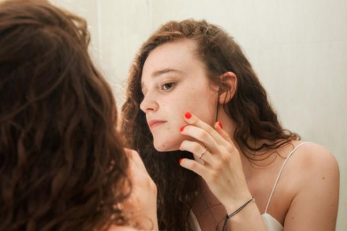 a teenager looking at her acne in front of the mirror 