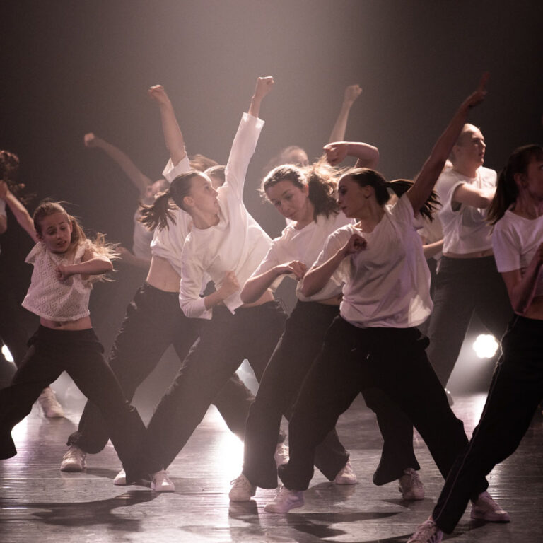 Girly Hip Hop dansers in een witte tshirt en zwarte broek tijdens een voorstelling van Ndigo.