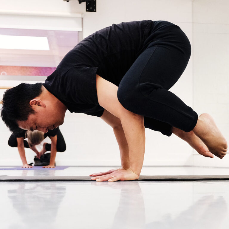 Een man in de crow pose tijdens een yoga les.